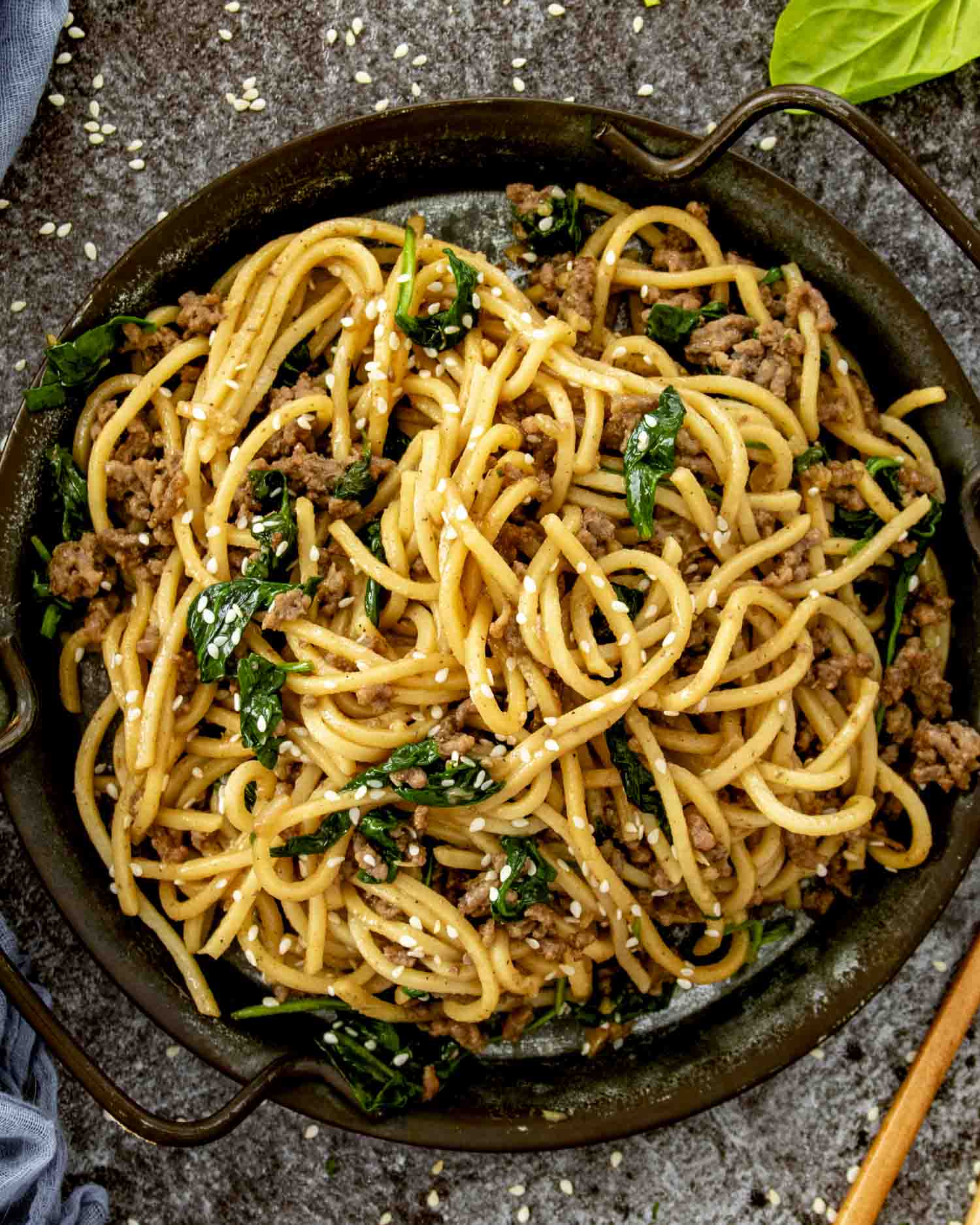 a serving of pork noodle stir fry in a brown metal plate.