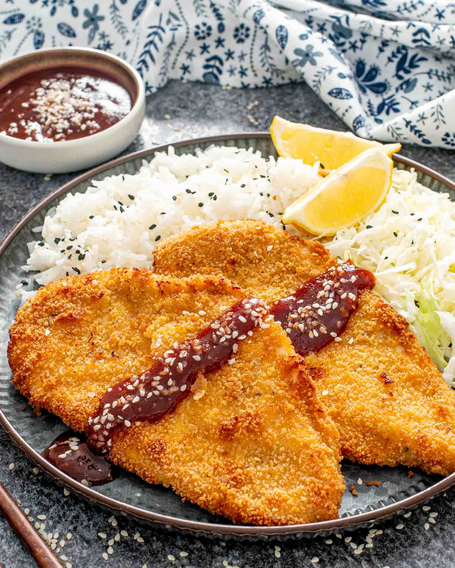 2 pieces of chicken katsu with tonkatsu sauce with rice and 2 lime wedges.