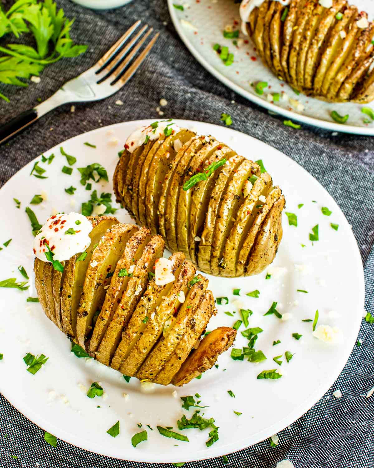 2 hasselback potatoes on a white plate garnished with sour cream and parsley.