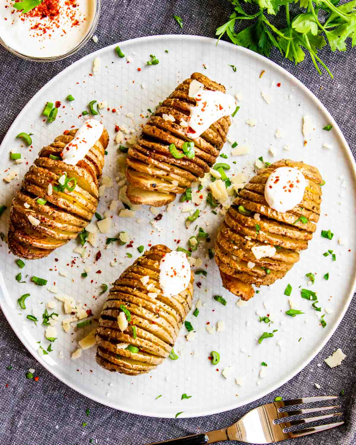 4 hasselback potatoes on a white plate with sour cream and parsley.