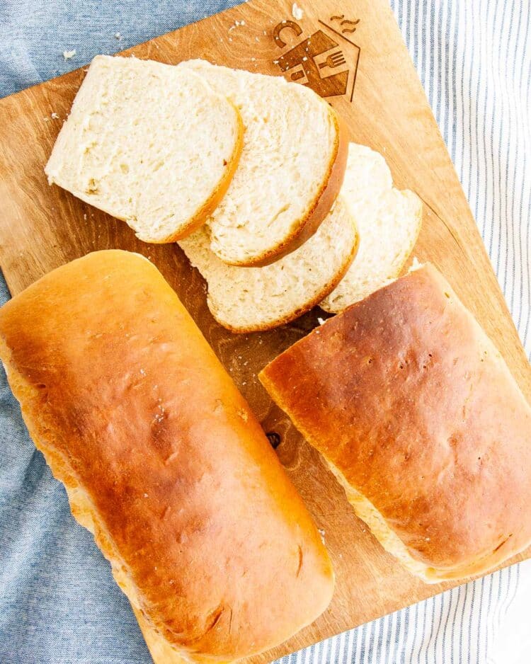 overhead shot of 2 amish white breads on a cutting board with one half cut into slices