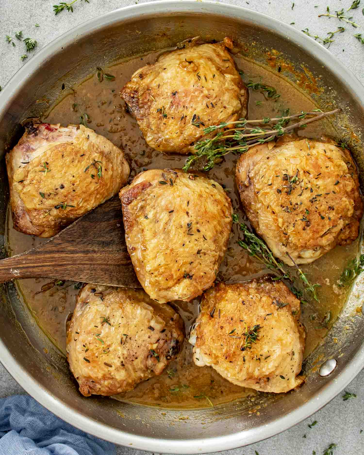 Skillet filled with golden, crispy chicken thighs nestled in apple cider glaze with thyme scattered throughout.