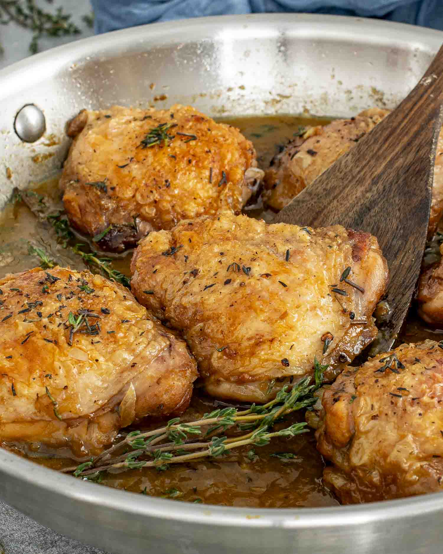 Crispy chicken thighs simmering in a rich apple cider sauce with thyme sprigs, cooked in a stainless-steel skillet.