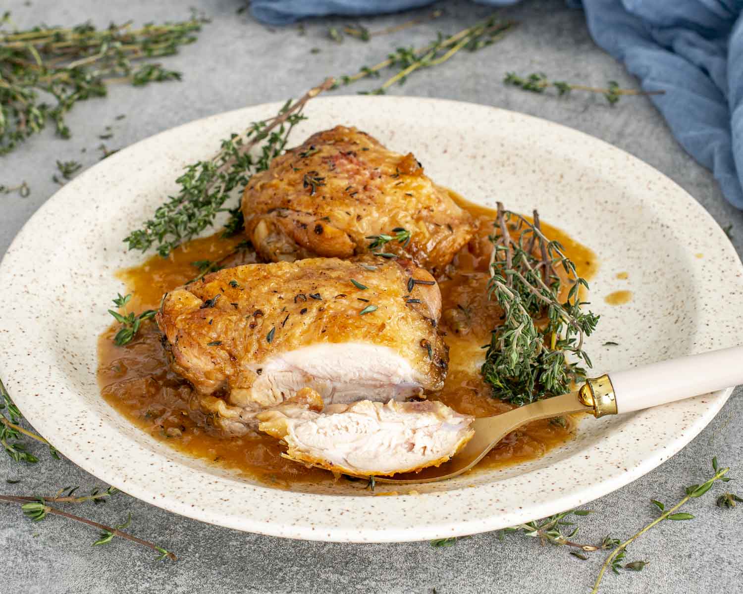 Juicy apple cider glazed chicken thigh sliced to show tender meat, served with thyme and plenty of glossy sauce.