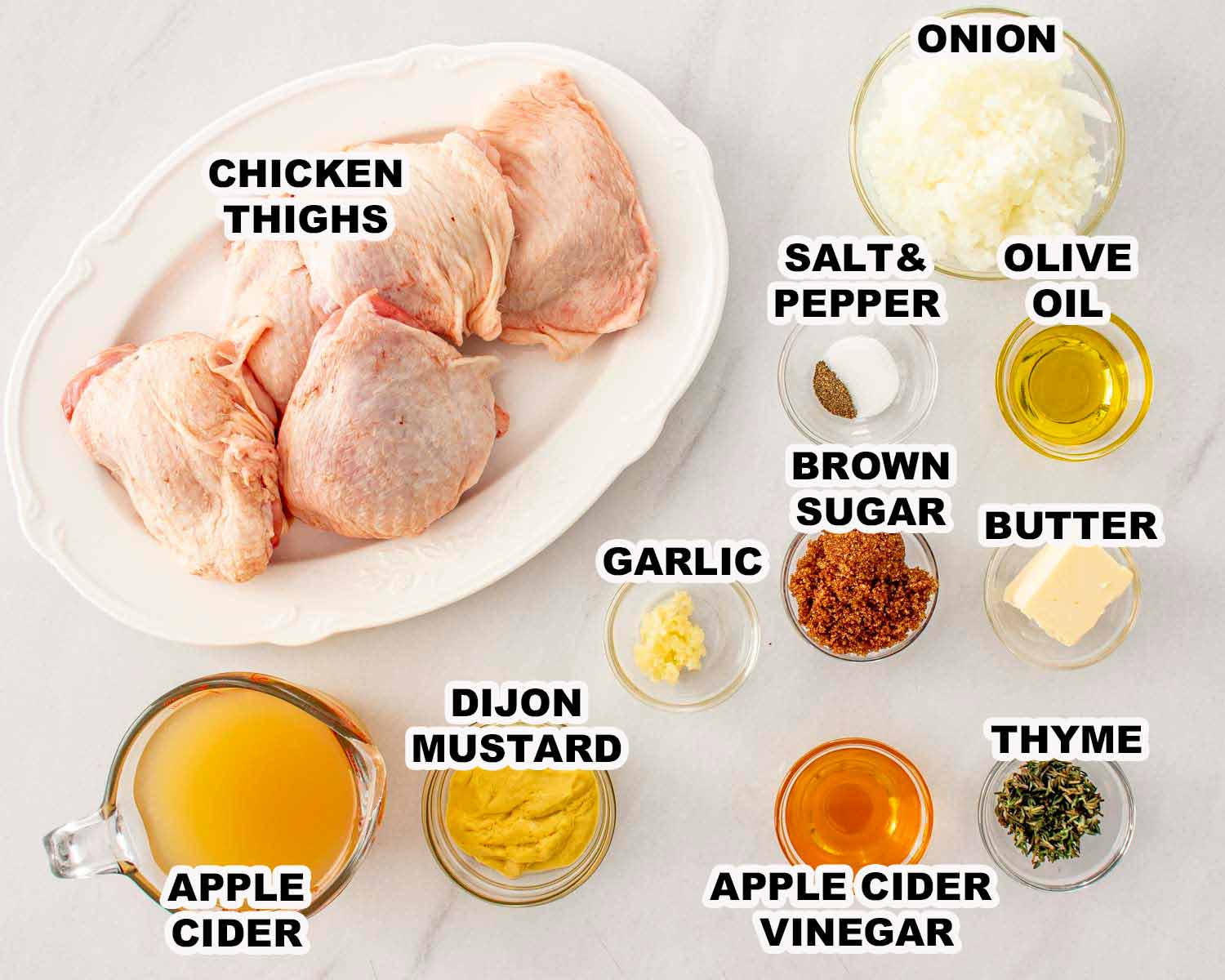 Chicken thighs, apple cider, Dijon, garlic, onion, brown sugar, vinegar, thyme, butter, and seasonings arranged for apple cider glazed chicken.