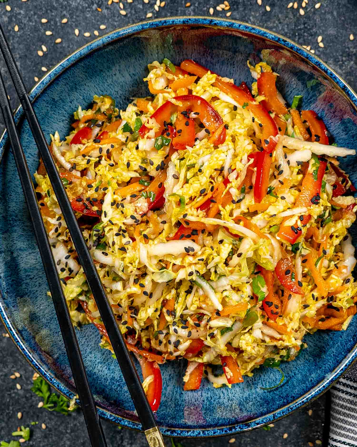 asian style slaw in a blue bowl garnished with sesame seeds.