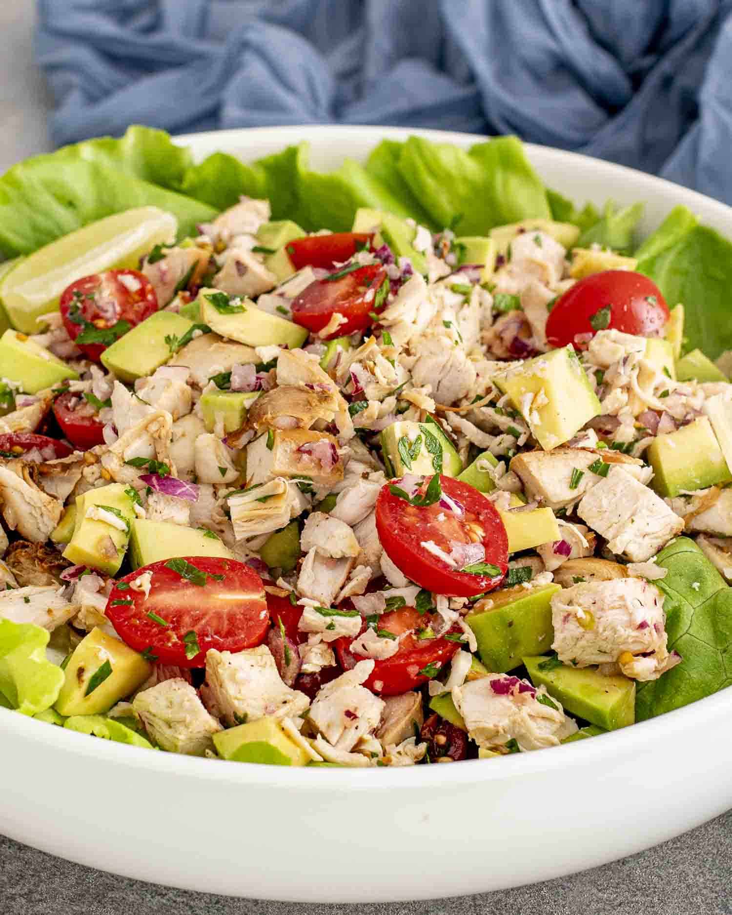 freshly made avocado chicken salad in a large white bowl on top of a bed of lettuce.