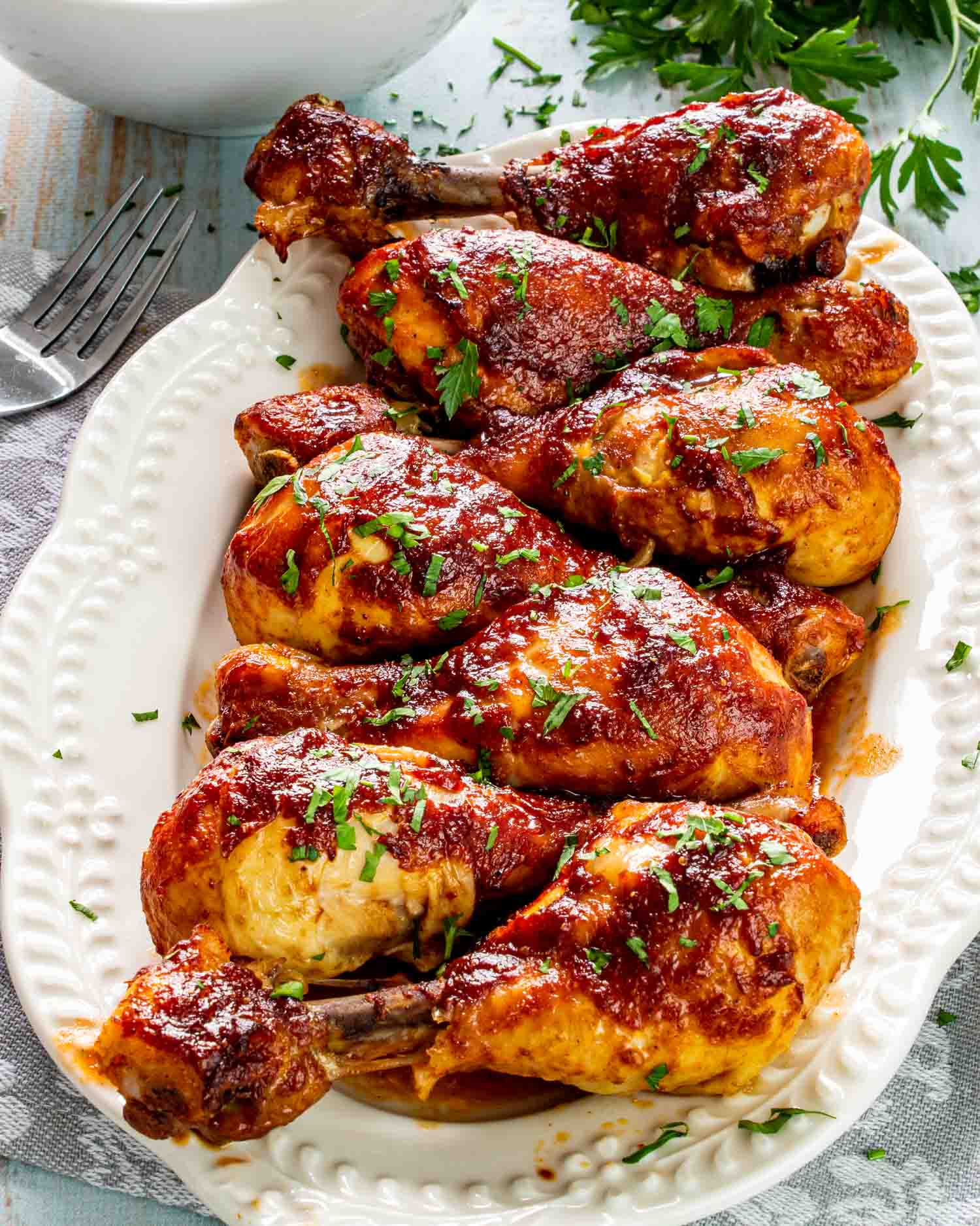 baked bbq chicken drumsticks on a white platter garnished with parsley.