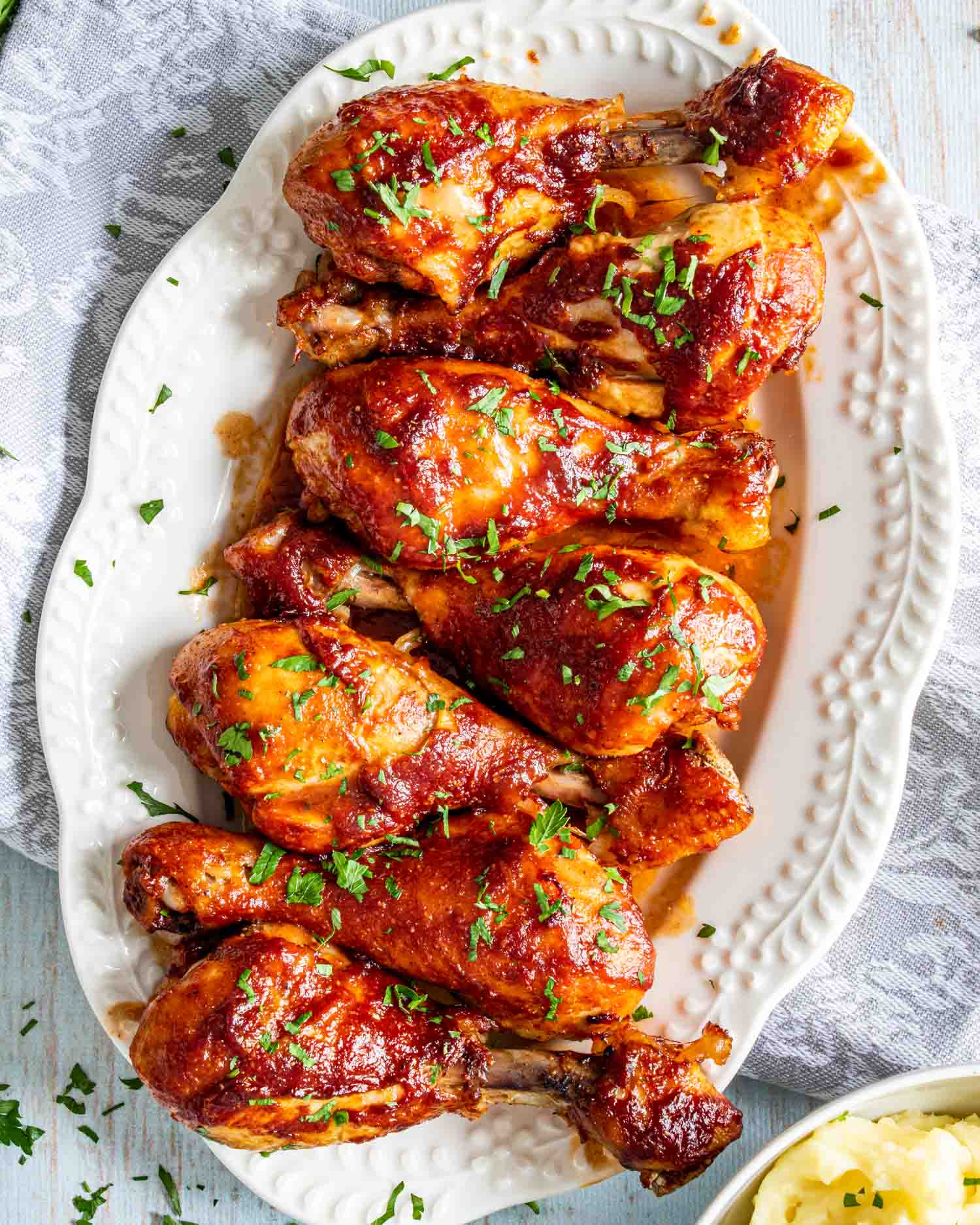 baked bbq chicken drumsticks on a white platter garnished with parsley.