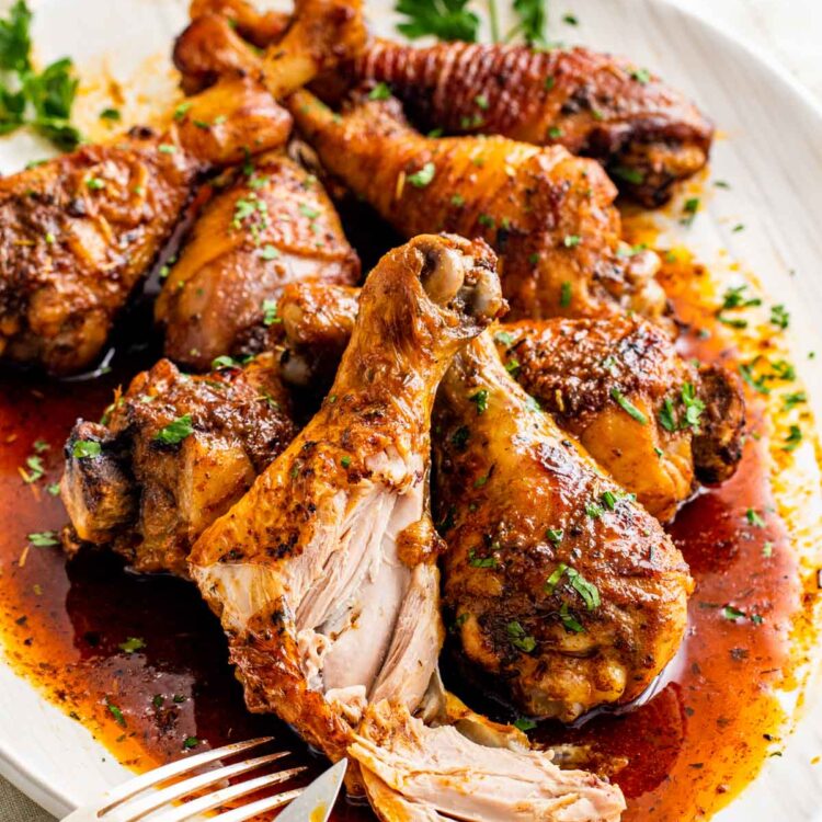 closeup of baked chicken drumsticks on a white serving platter with sauce from pan.