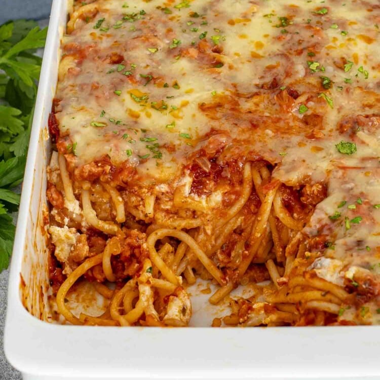 baked spaghetti garnished with parsley in a white casserole dish.