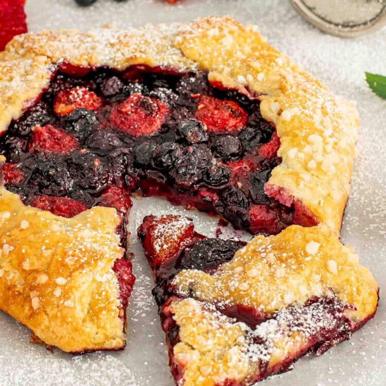 a berry galette with one slice cut out on a white surface.