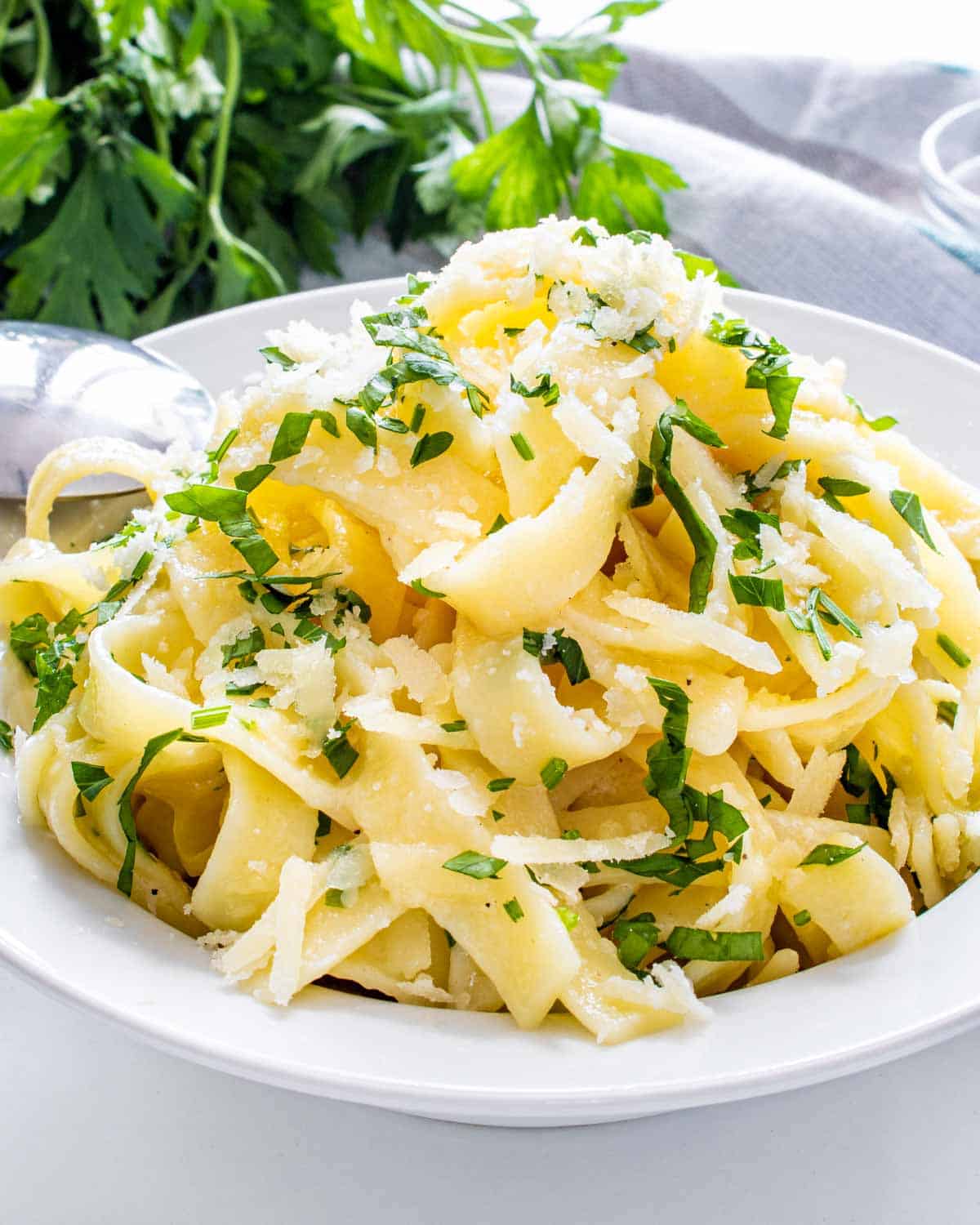 buttered noodles garnished with parsley on a white plate.