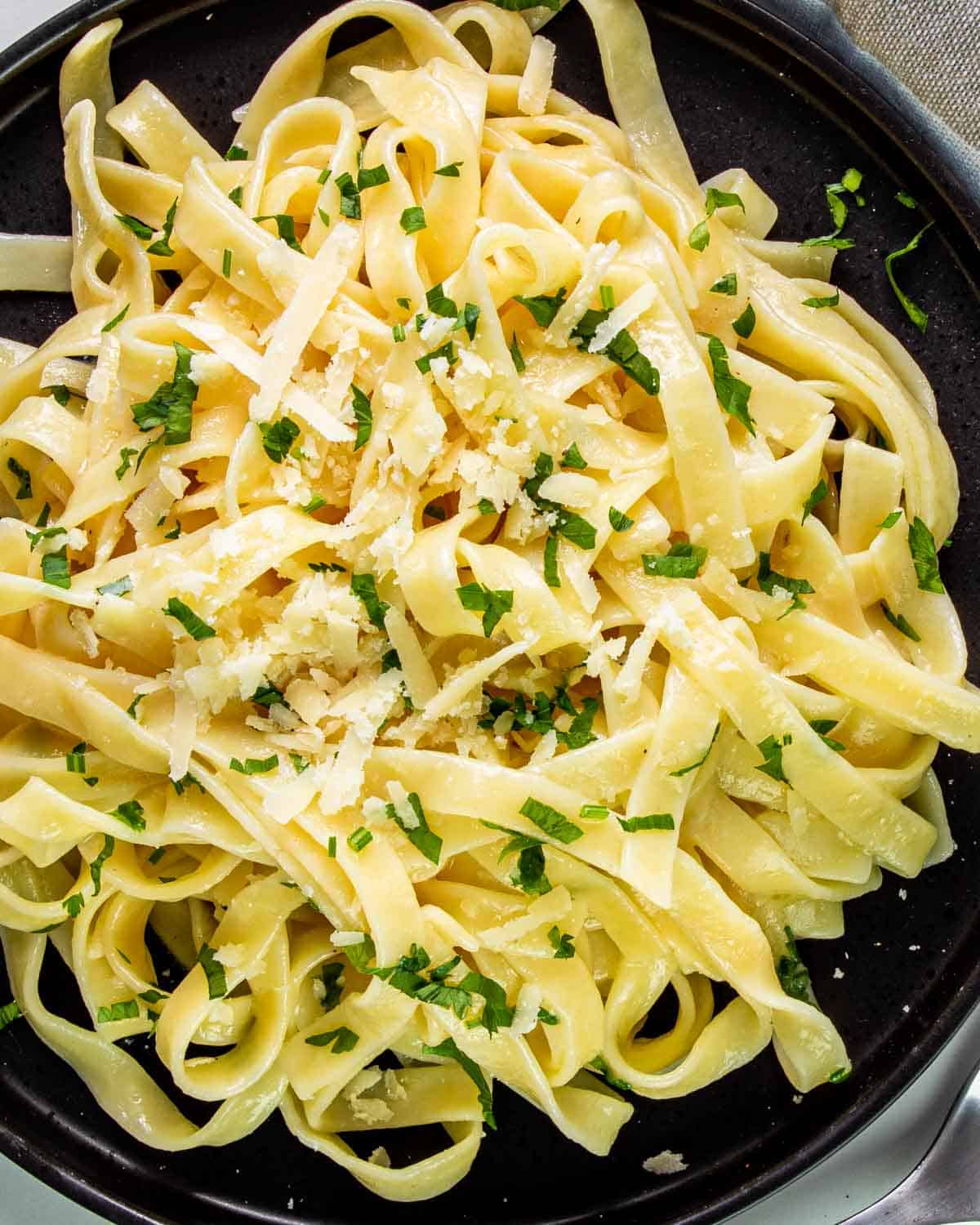 buttered noodles garnished with parsley on a black plate.