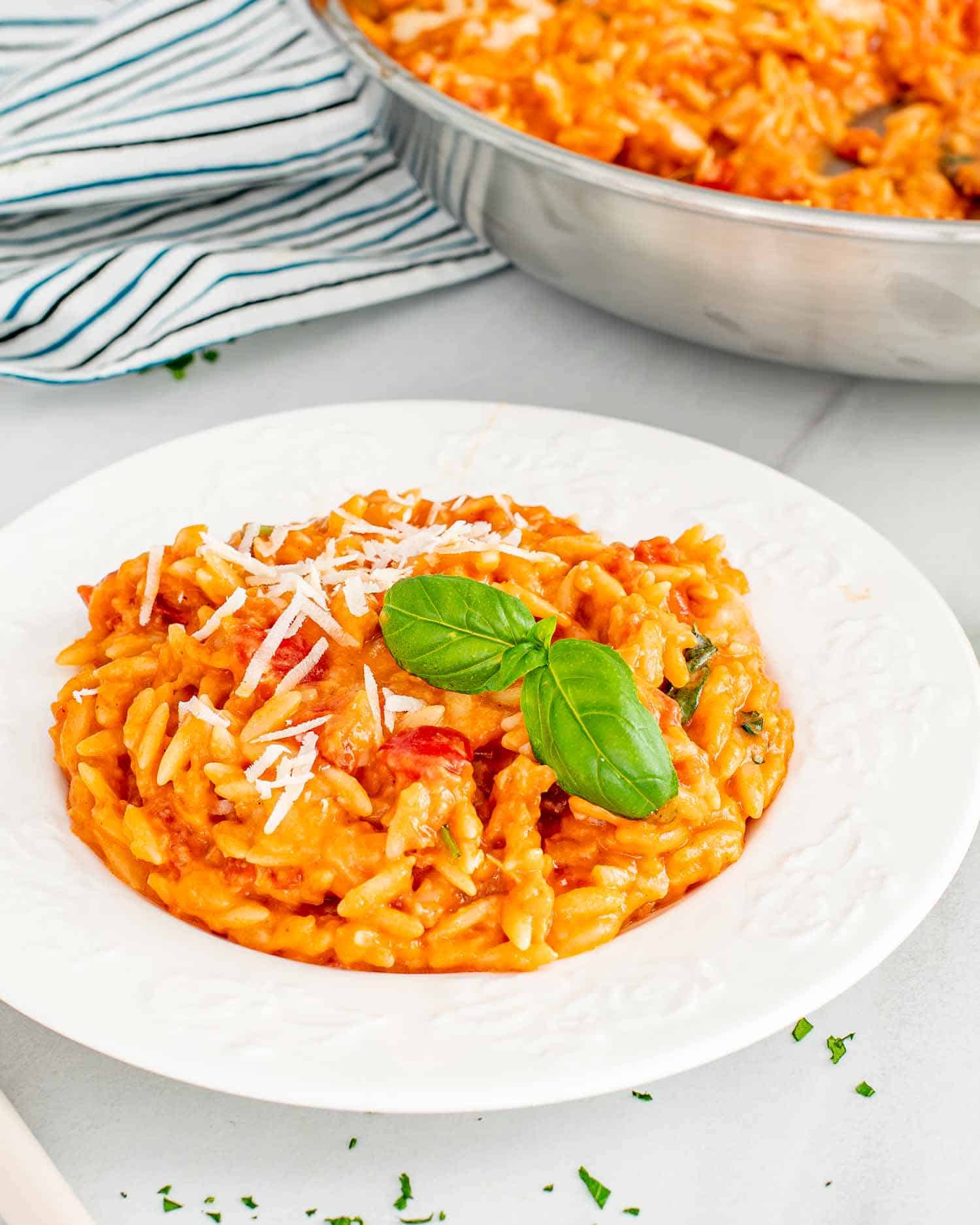 a serving of cheesy tomato basil orzo on a white plate.