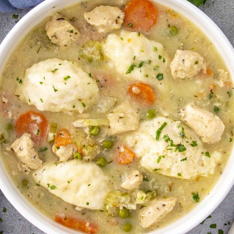 Bowl of chicken and dumplings with tender chicken, vegetables, and fluffy dumplings in a creamy broth, garnished with parsley.