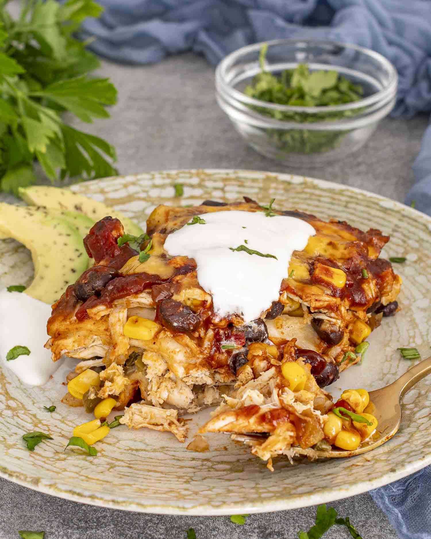 a slice of chicken enchilada casserole on a plate with a dollop of sour cream.