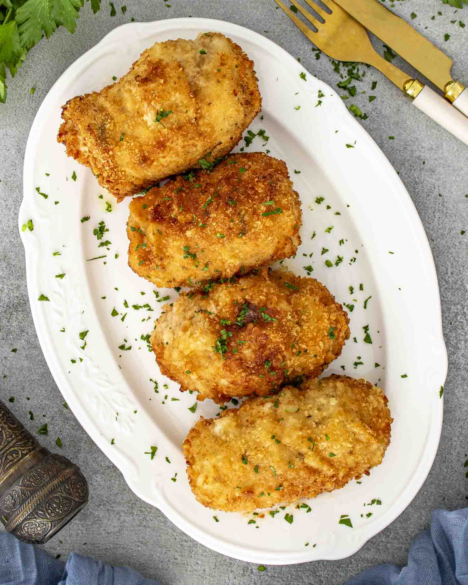 Four golden brown Chicken Kiev rolls on a white platter, garnished with chopped parsley for serving.