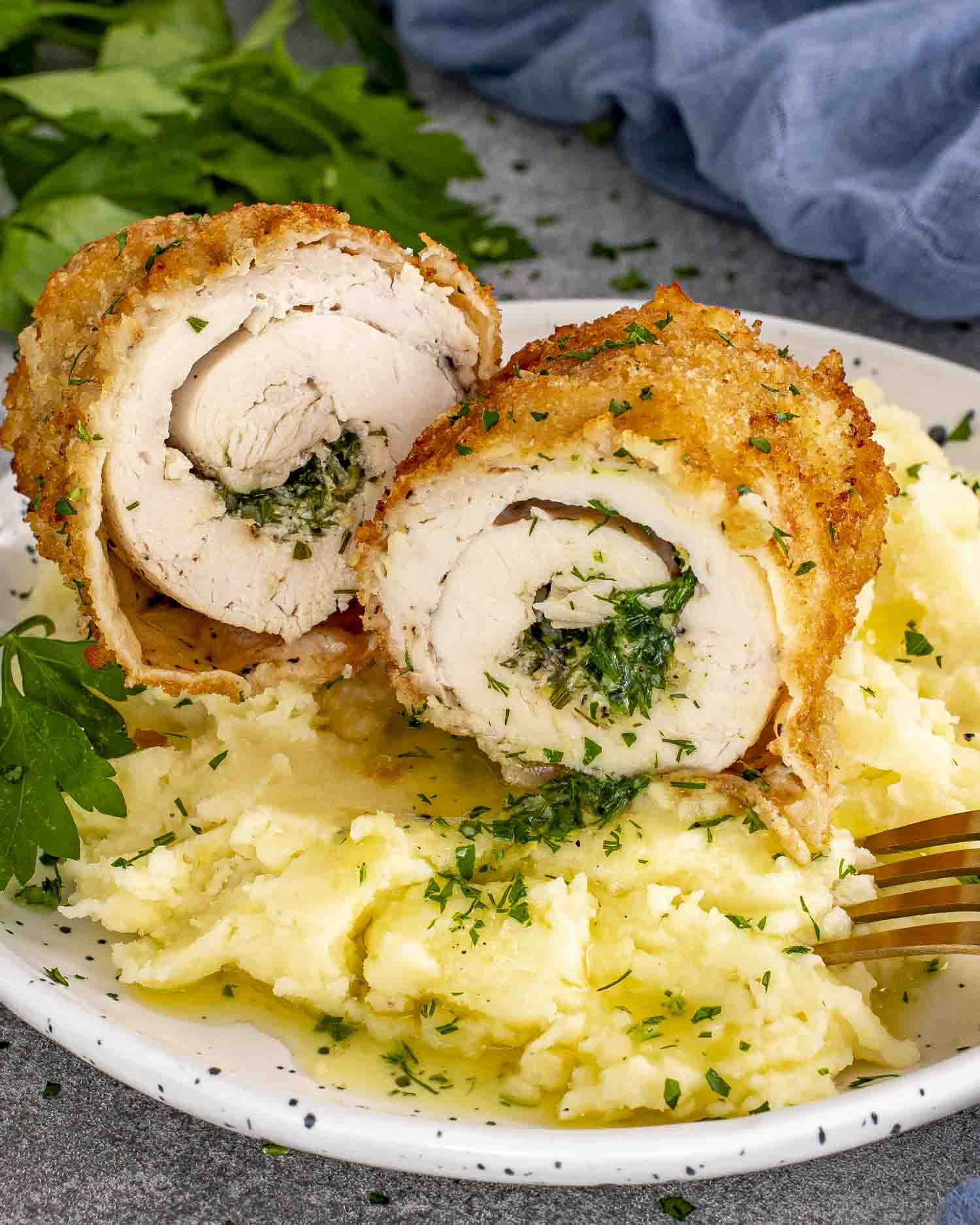 Sliced Chicken Kiev showing garlic herb butter center, served over creamy mashed potatoes, sprinkled with parsley.
