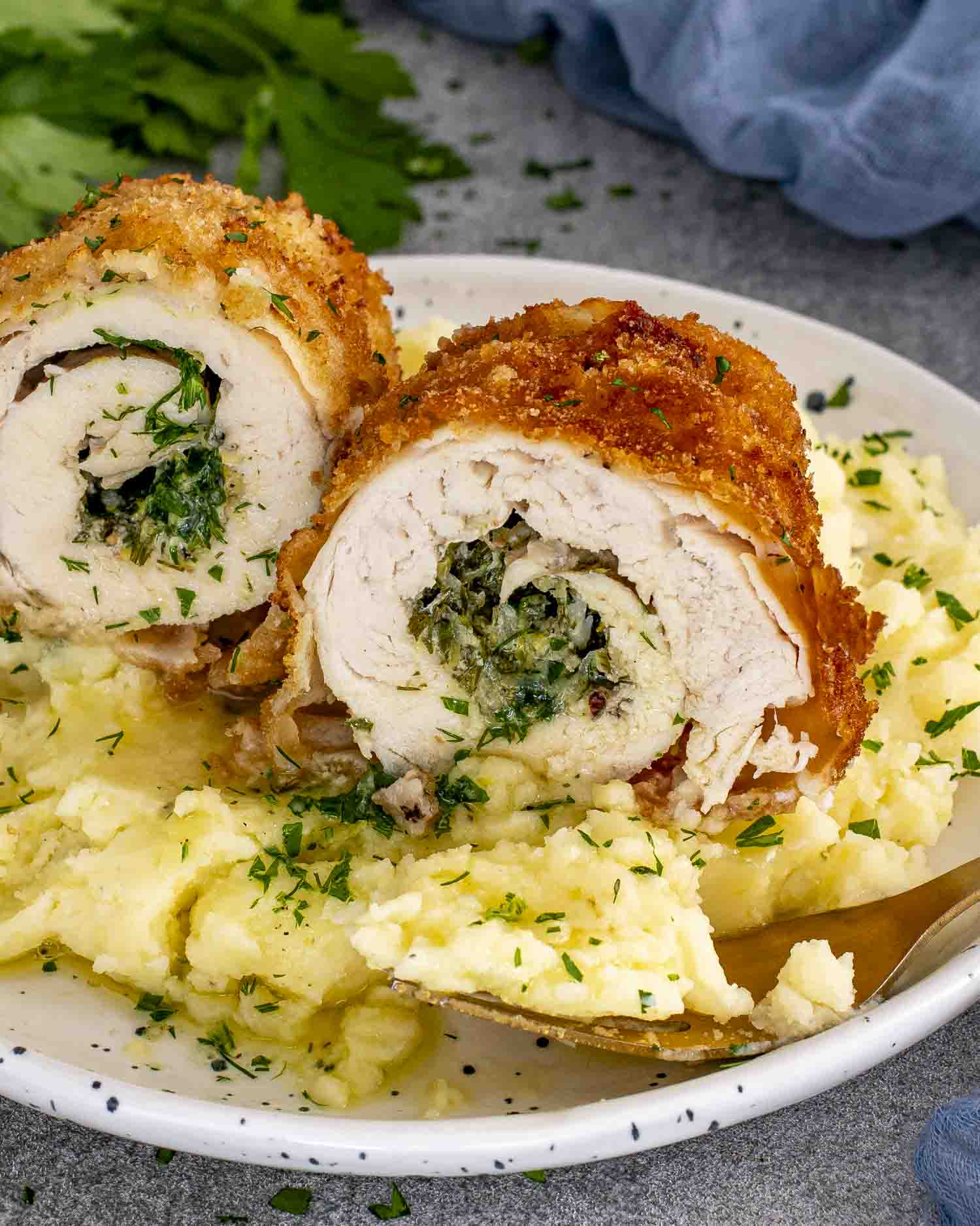 Sliced Chicken Kiev showing garlic herb butter center, served over creamy mashed potatoes, sprinkled with parsley.
