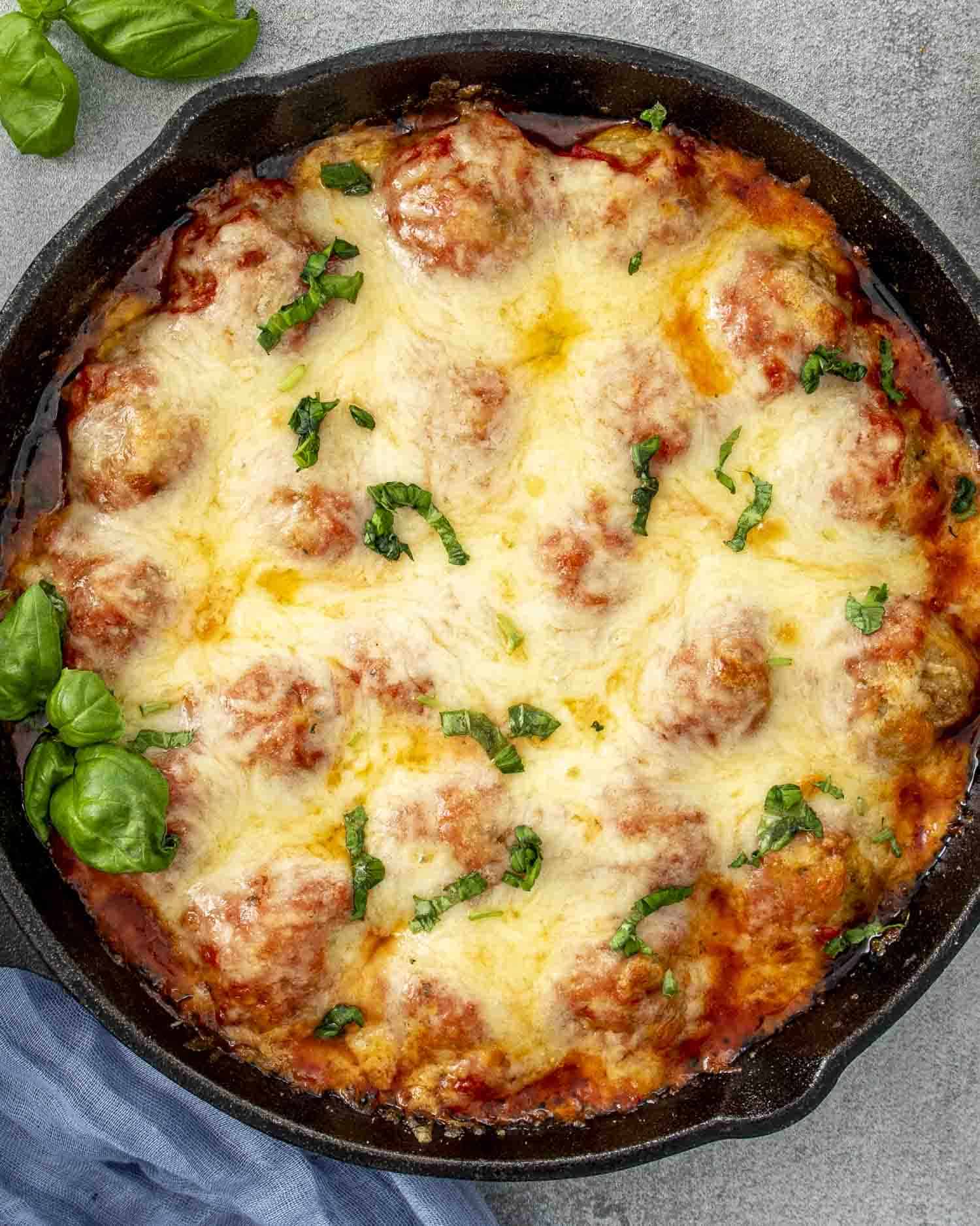 fresh out of the oven chicken parmesan meatballs in a cast iron skillet garnished with some fresh basil.