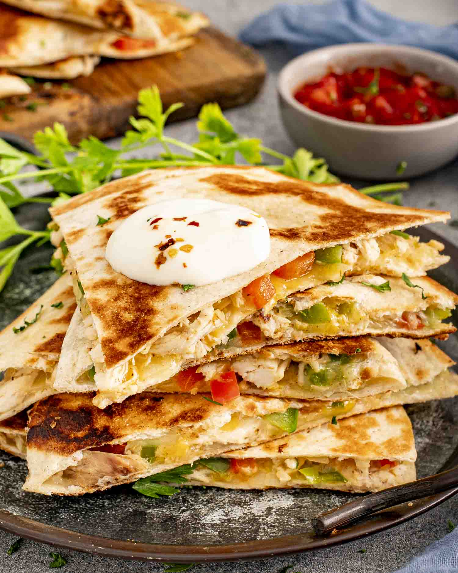 a stack of chicken quesadillas on a board with a bowl of salsa in the background.
