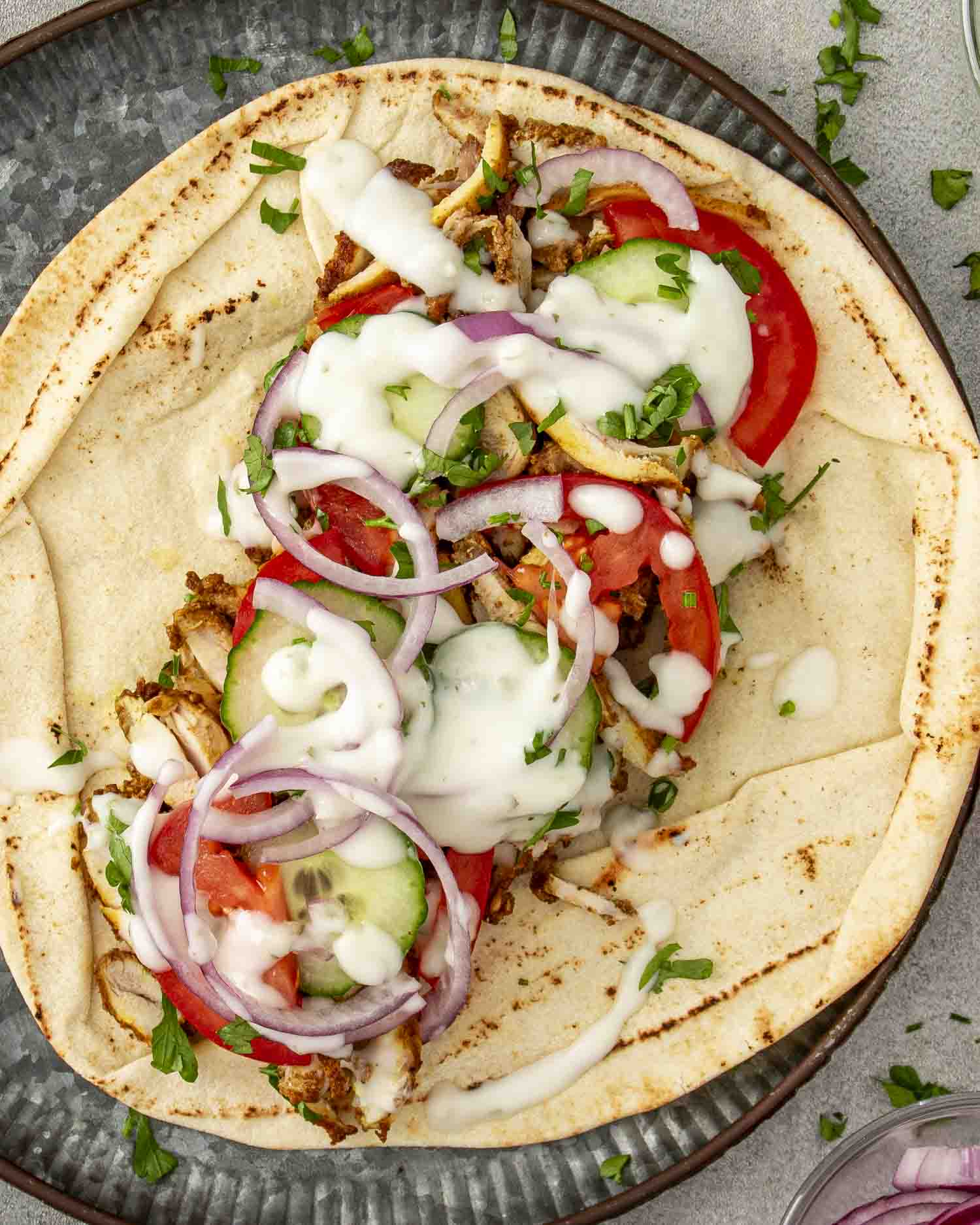 An open Chicken Shawarma wrap with grilled chicken, sliced tomatoes, cucumbers, red onions, and topped with tzatziki sauce.