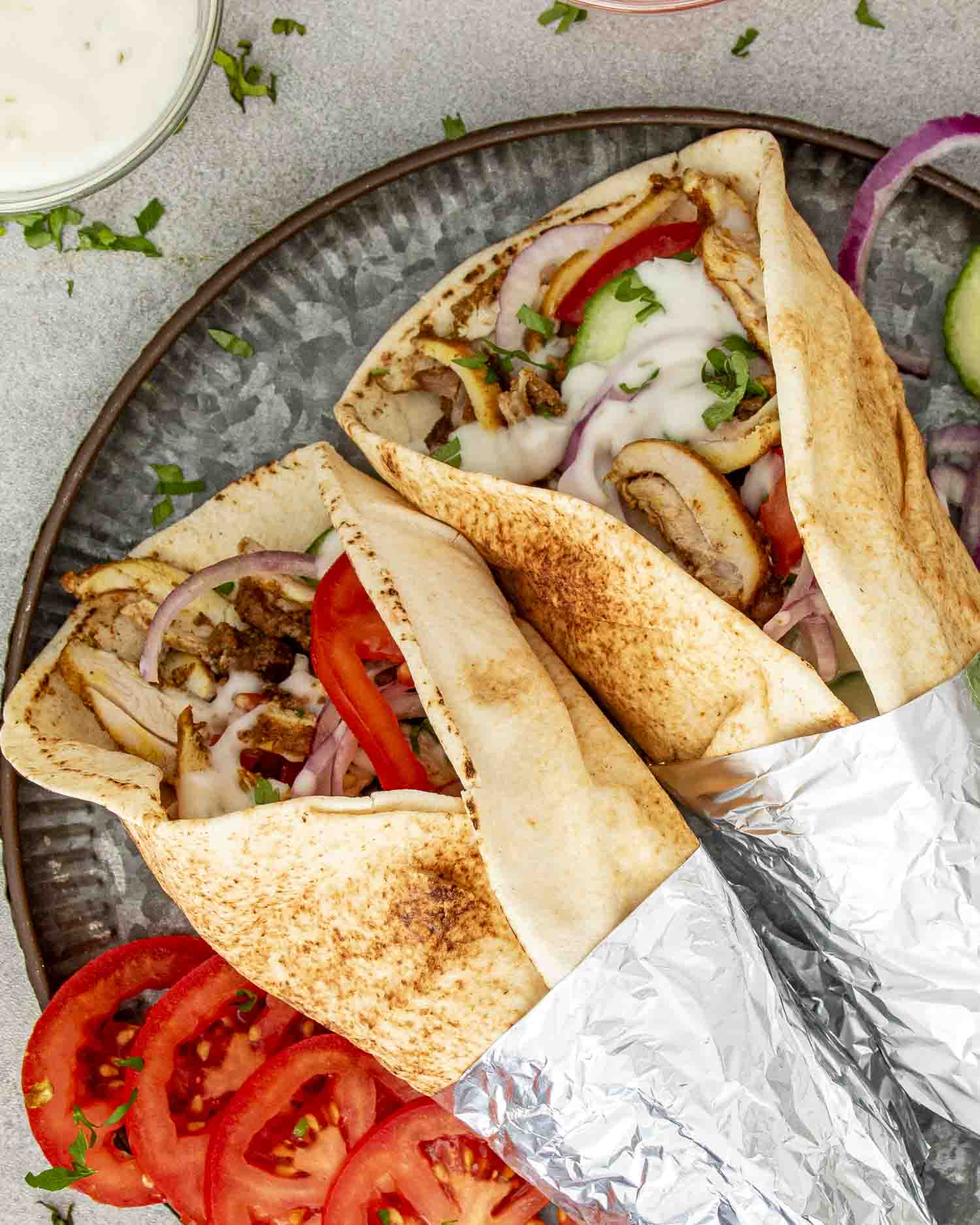 Two Chicken Shawarma wraps in pita bread, filled with juicy chicken, tomatoes, red onions, and drizzled with tzatziki sauce.