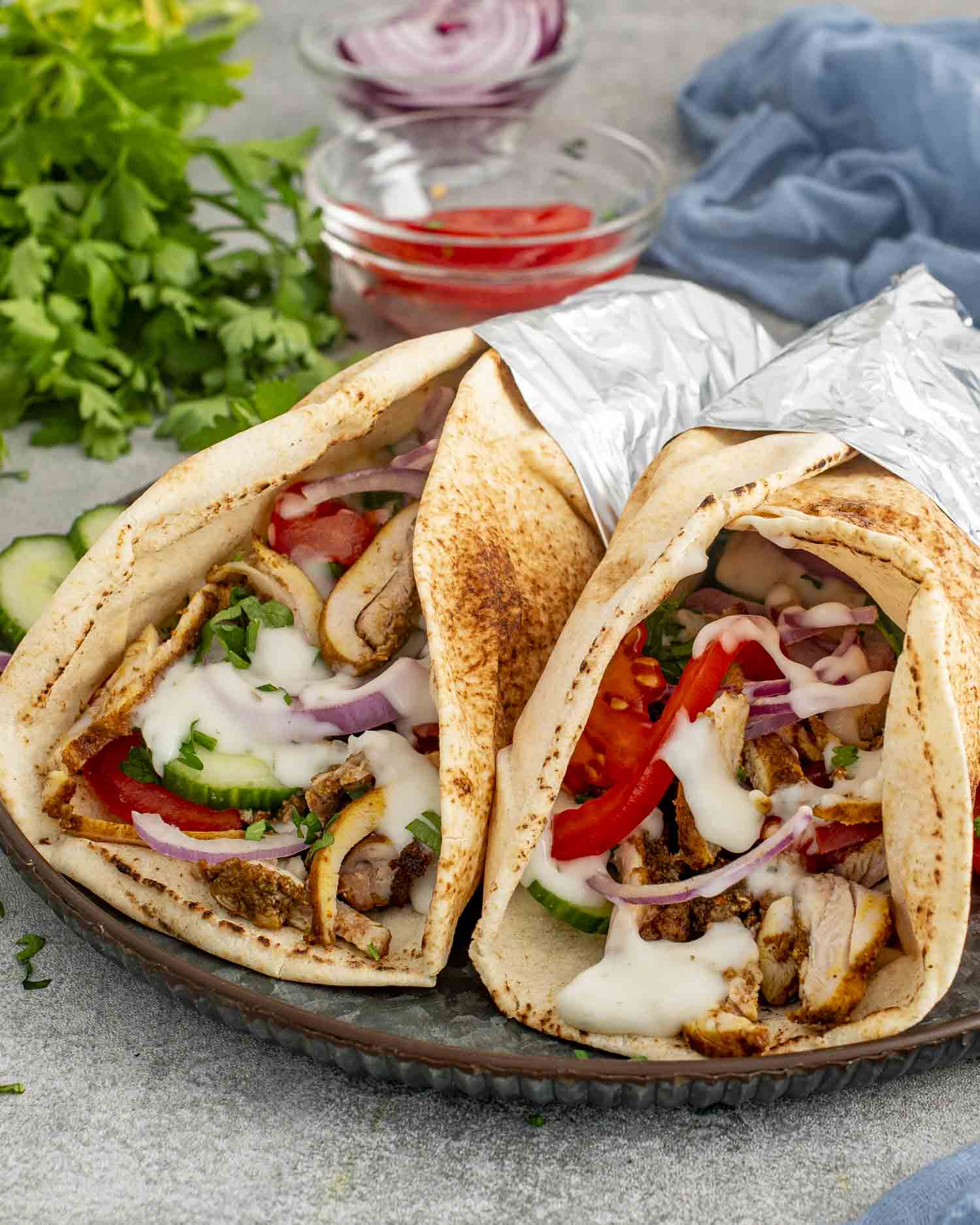 Two Chicken Shawarma wraps in pita bread, filled with juicy chicken, tomatoes, red onions, and drizzled with tzatziki sauce.