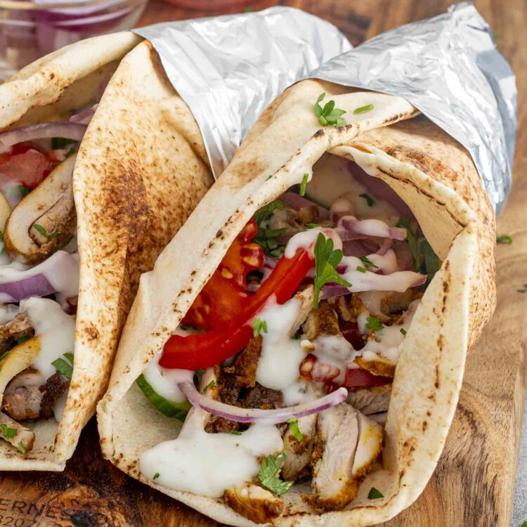 Two Chicken Shawarma wraps in pita bread, filled with juicy chicken, tomatoes, red onions, and drizzled with tzatziki sauce.