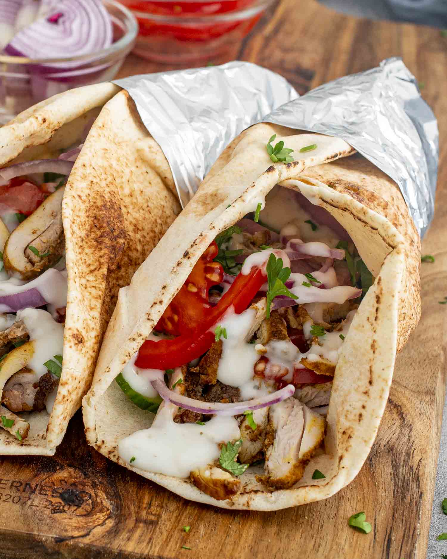 Two Chicken Shawarma wraps in pita bread, filled with juicy chicken, tomatoes, red onions, and drizzled with tzatziki sauce.