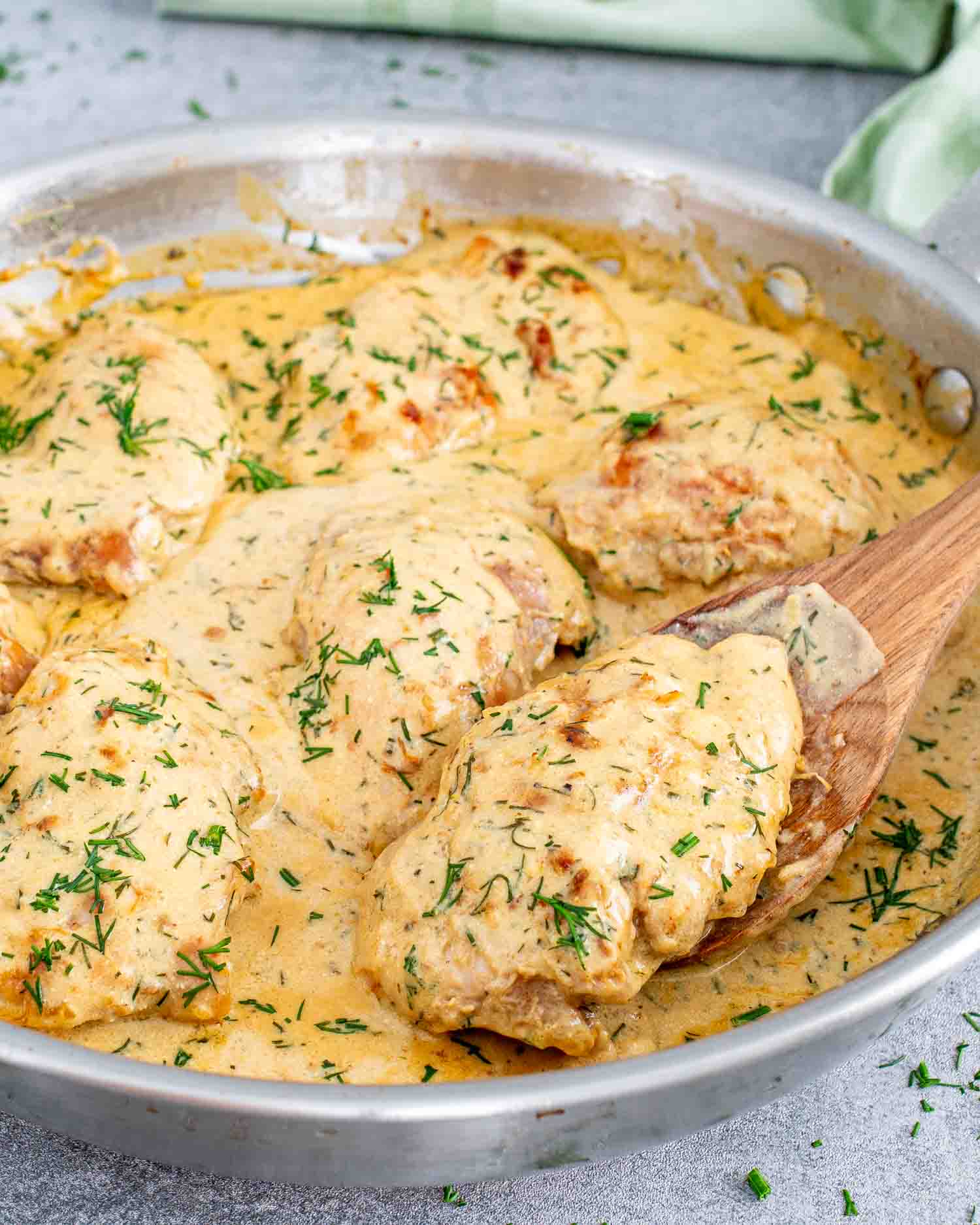chicken thighs with creamy lemon dill sauce in a skillet with a spoon.