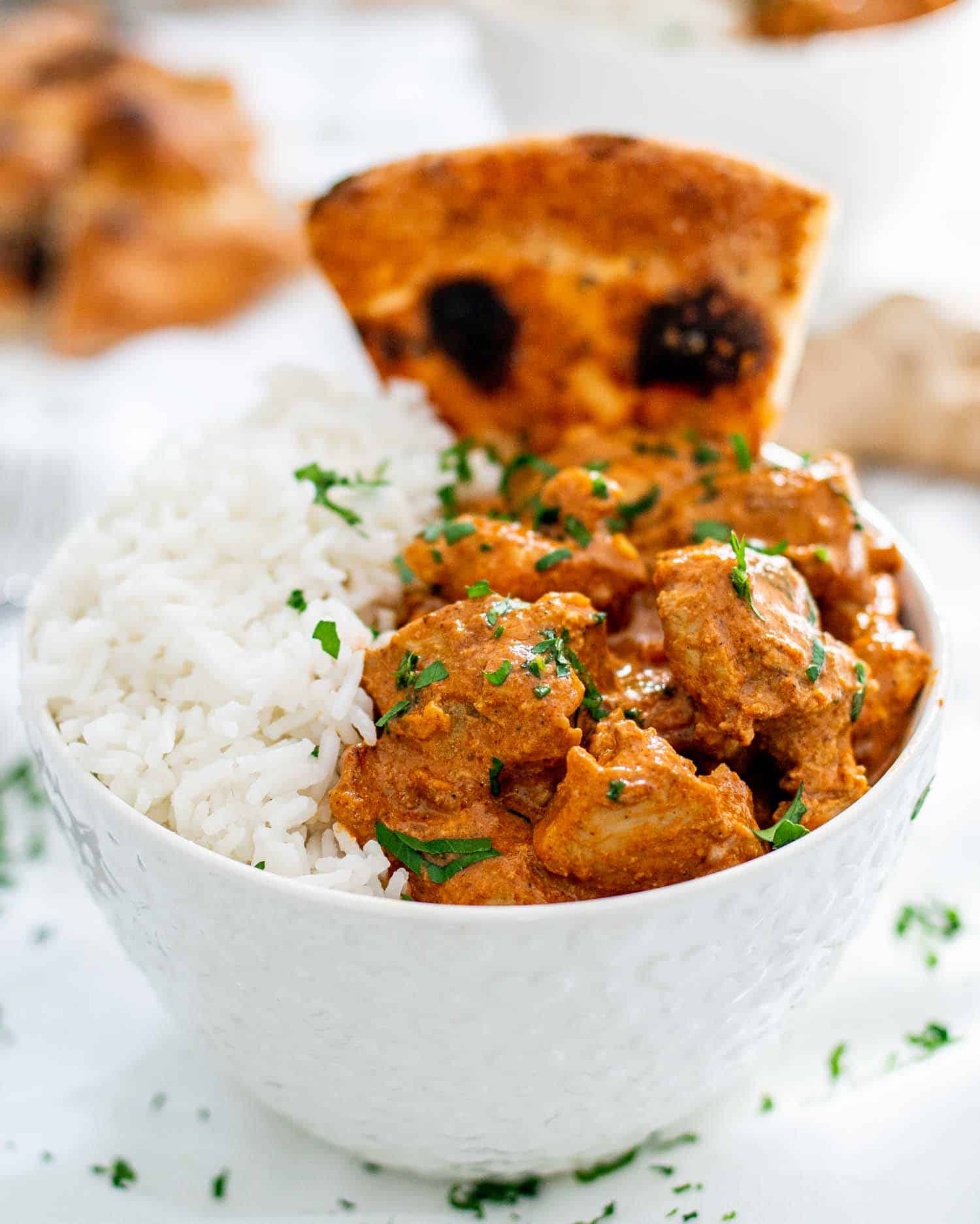 chicken tikka masala with rice in a white bowl and a piece of naan.
