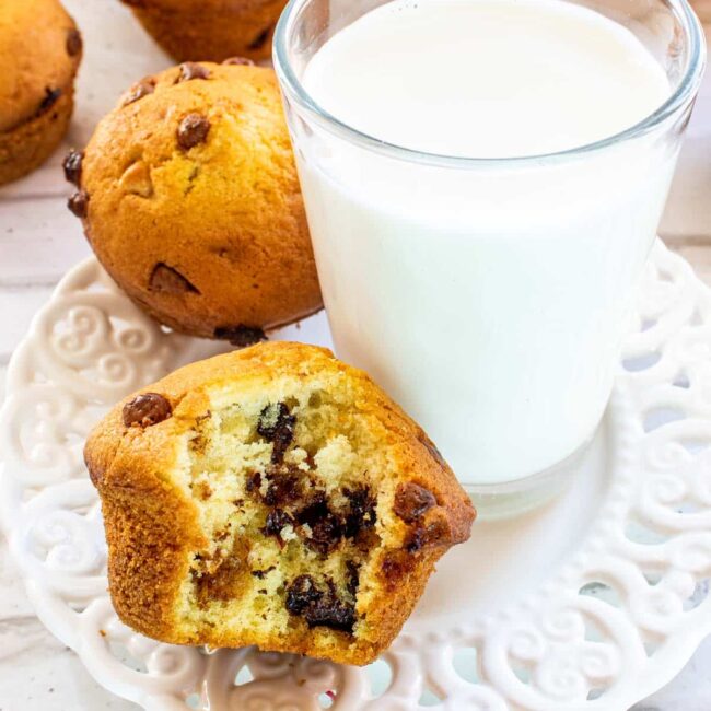 half eaten muffin on a white plate with a glass of milk.