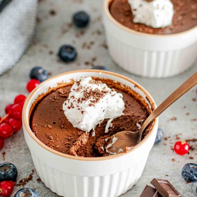Chocolate pots de crème topped with whipped cream, garnished with fresh berries and chocolate shavings.