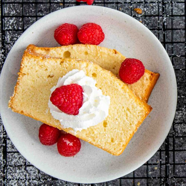 a couple slices of condensed milk pound cake on a dessert plate garnished with raspberries.