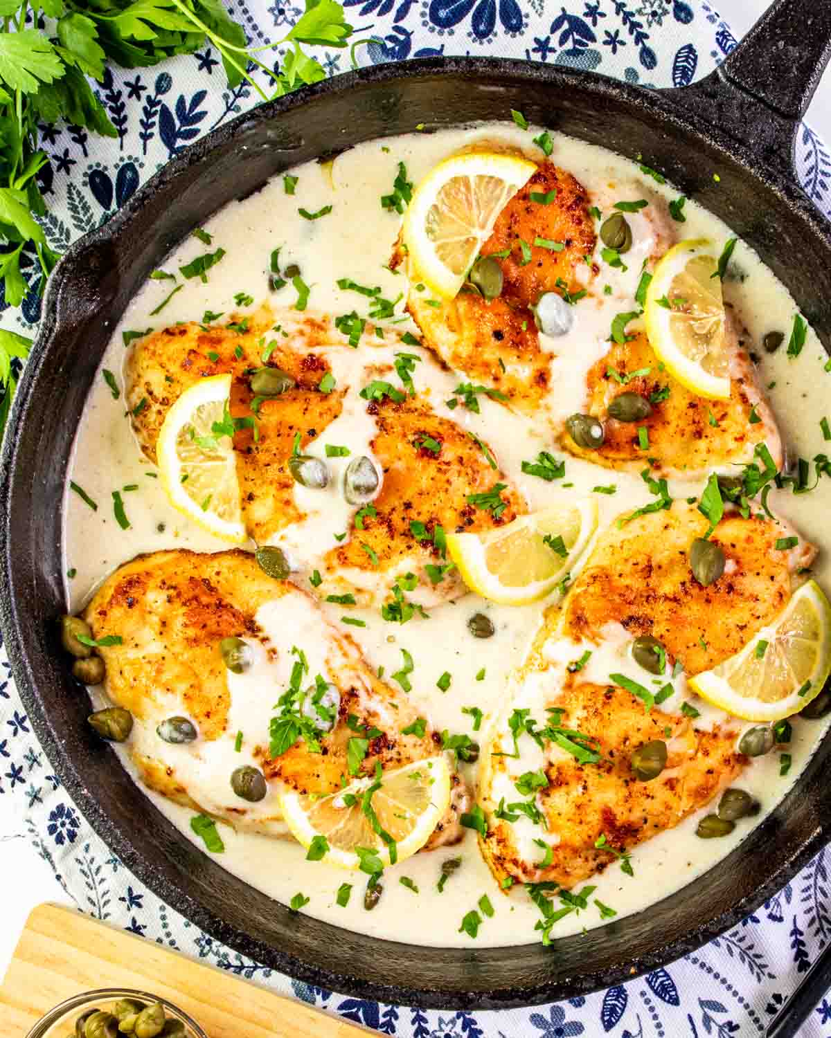 creamy chicken piccata in a black cast iron skillet garnished with parsley and lemon wedges.