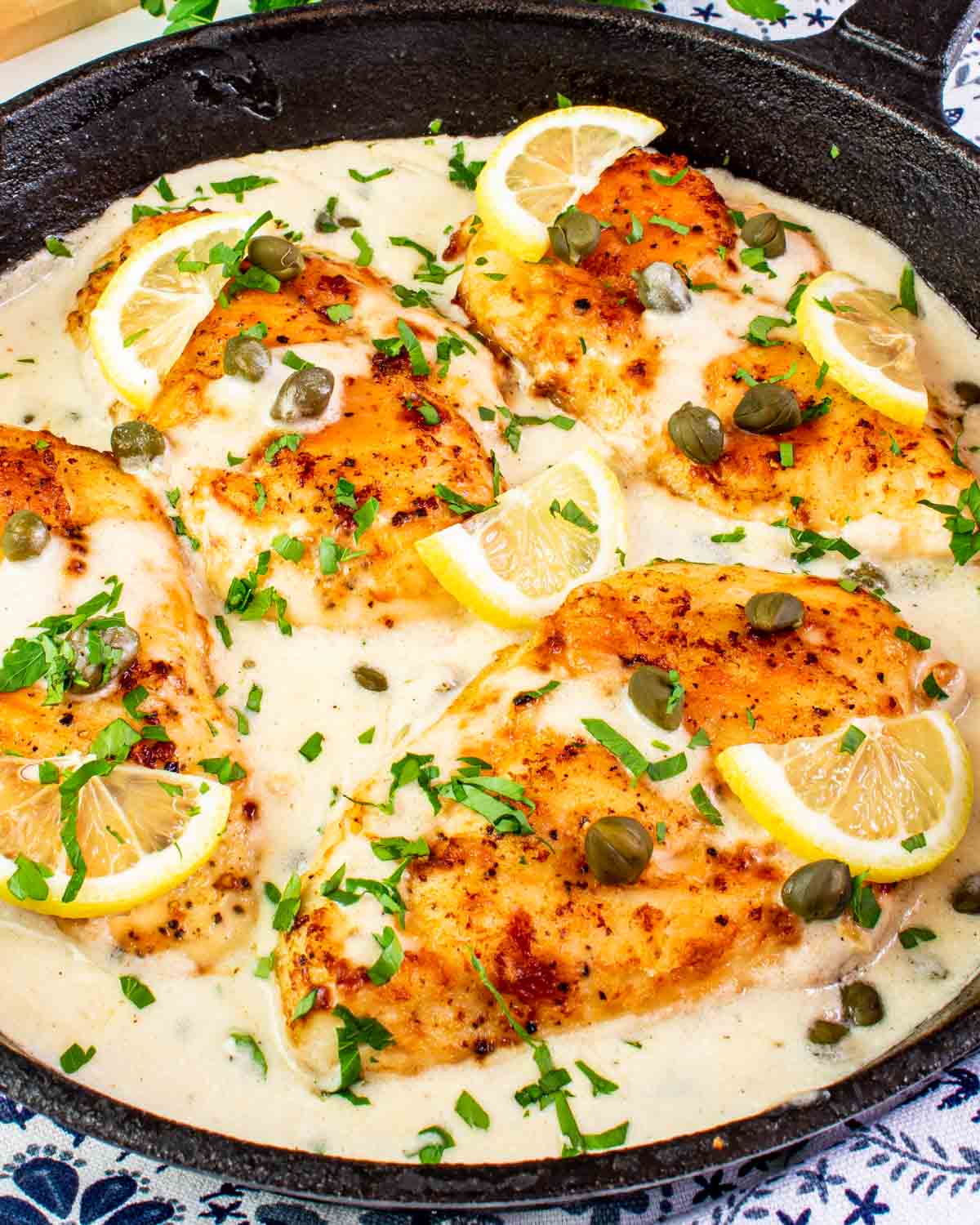 creamy chicken piccata in a black cast iron skillet garnished with parsley and lemon wedges.