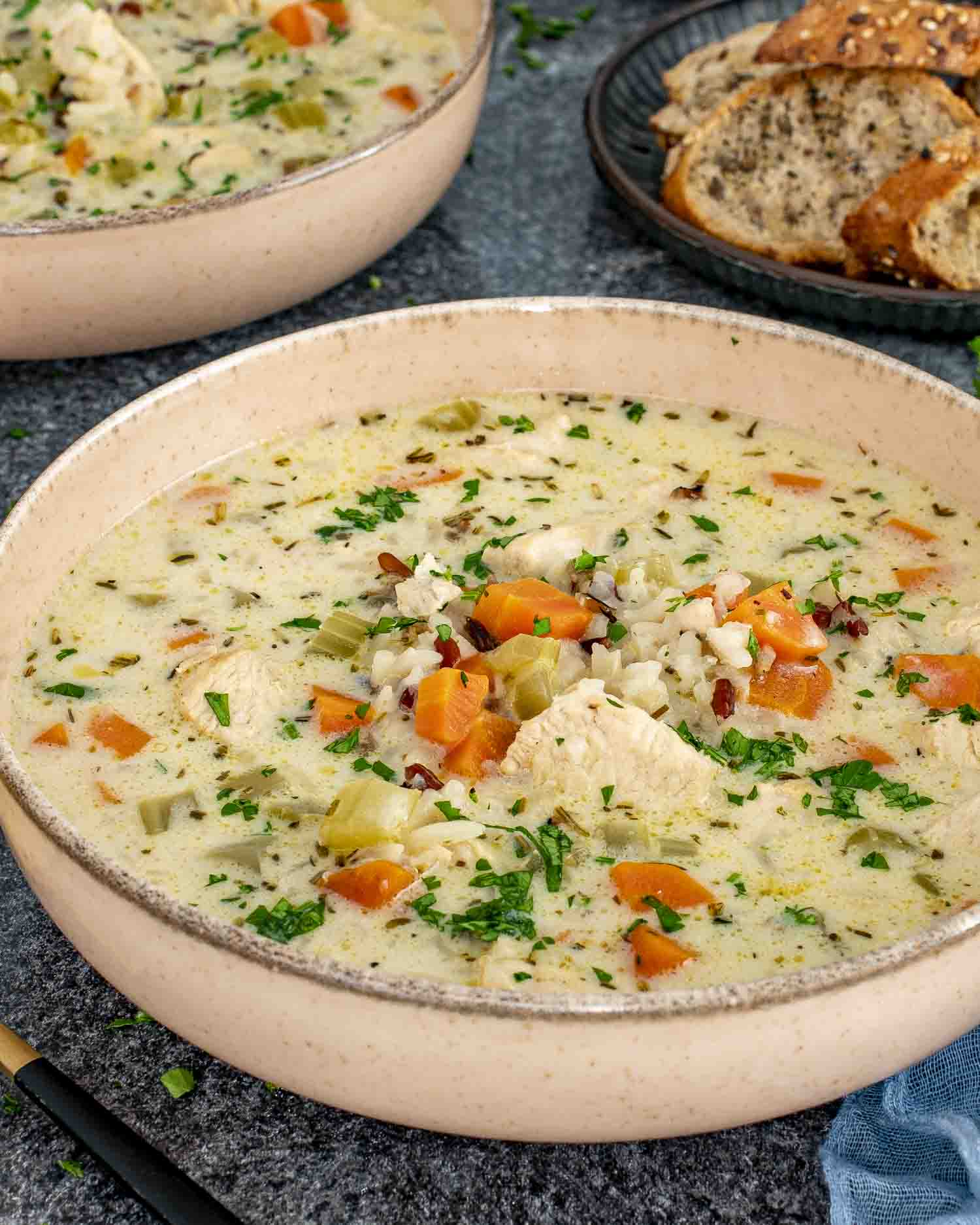 A warm, comforting bowl of creamy chicken wild rice soup, filled with tender chunks of chicken, diced carrots, celery, and wild rice in a rich, herb-infused broth.