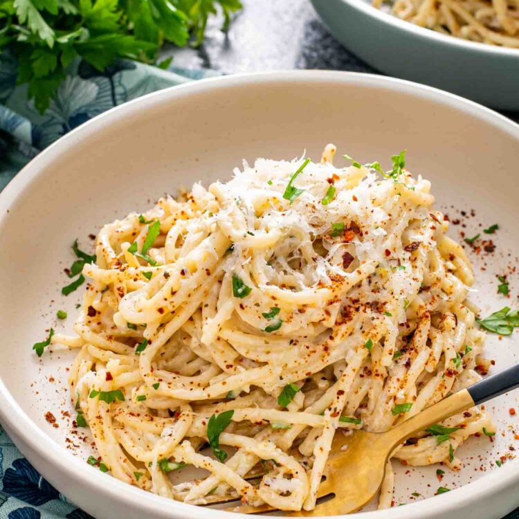 garlic butter spaghetti in a white bowl garnished with parsley and red pepper flakes.