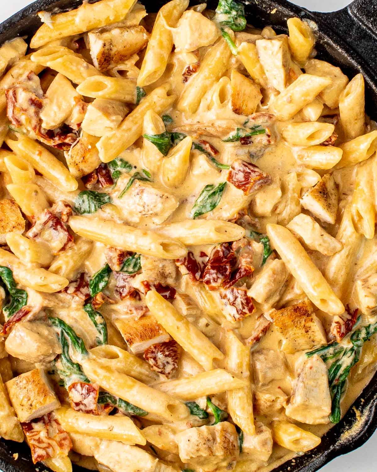 creamy tuscan chicken pasta in a black skillet.