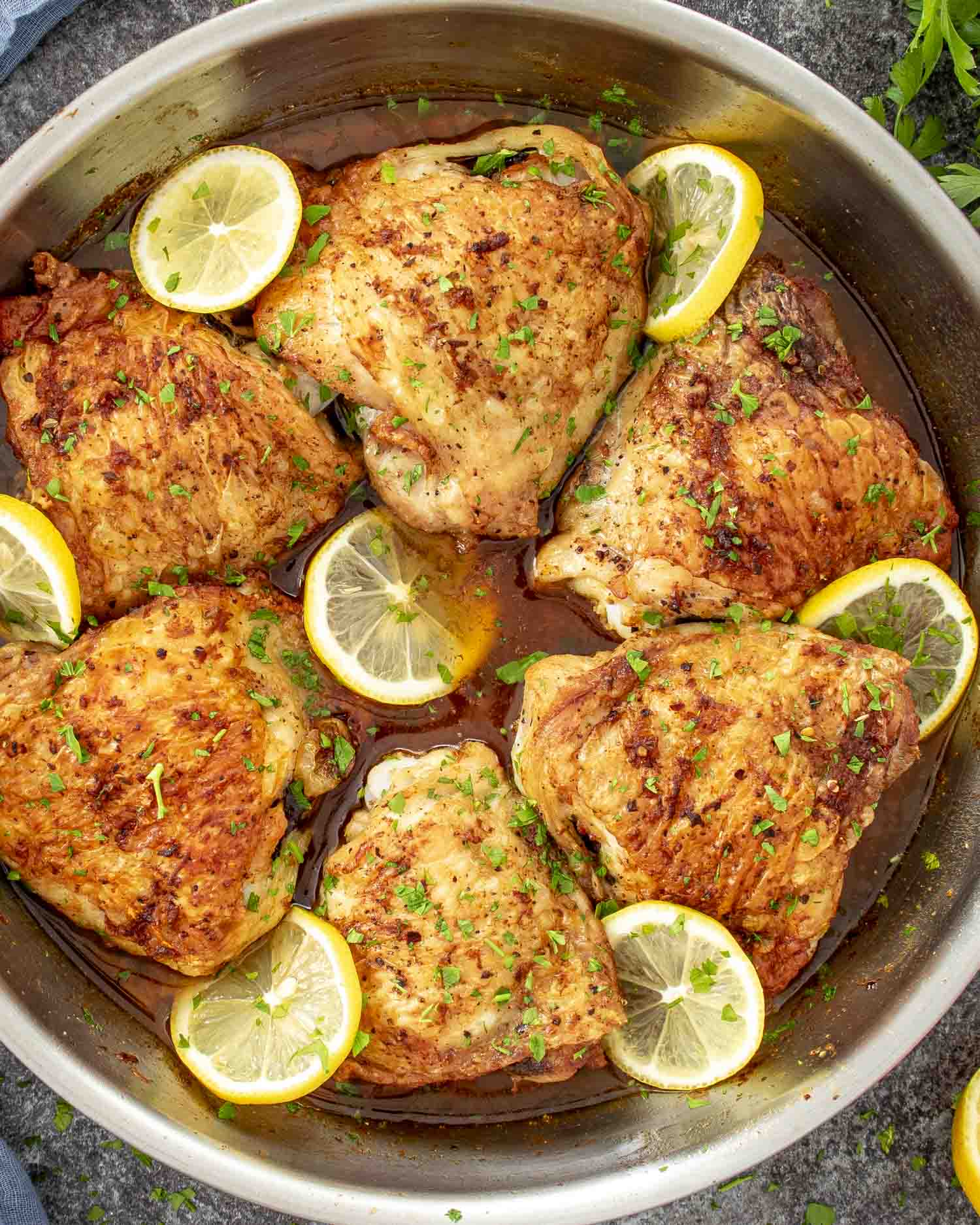 crispy lemon chicken thighs fresh out of the oven in a skillet garnished with parsley and lemon slices.