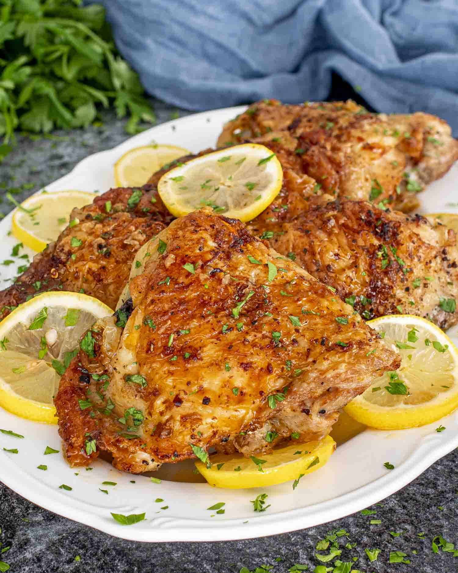crispy lemon chicken thighs garnished with parsley and lemon slices on a white serving platter.