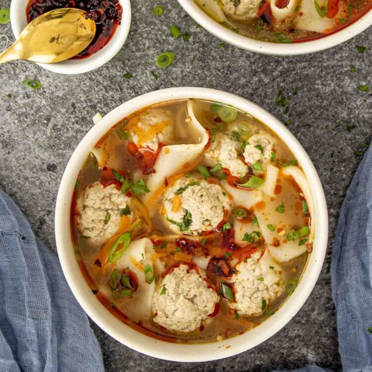 a beige bowl loaded with deconstructed wonton soup and garnished with chili oil.