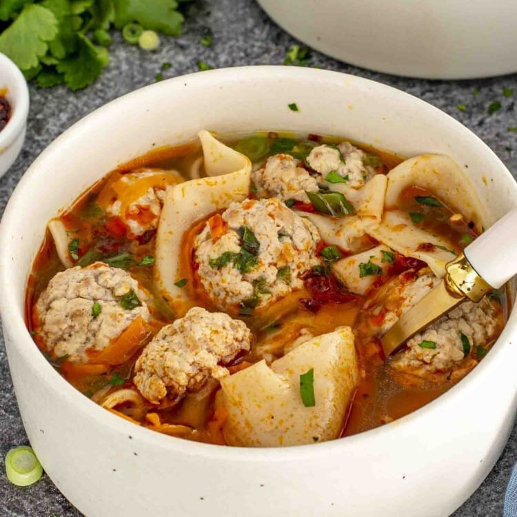 a beige bowl loaded with deconstructed wonton soup and garnished with chili oil.