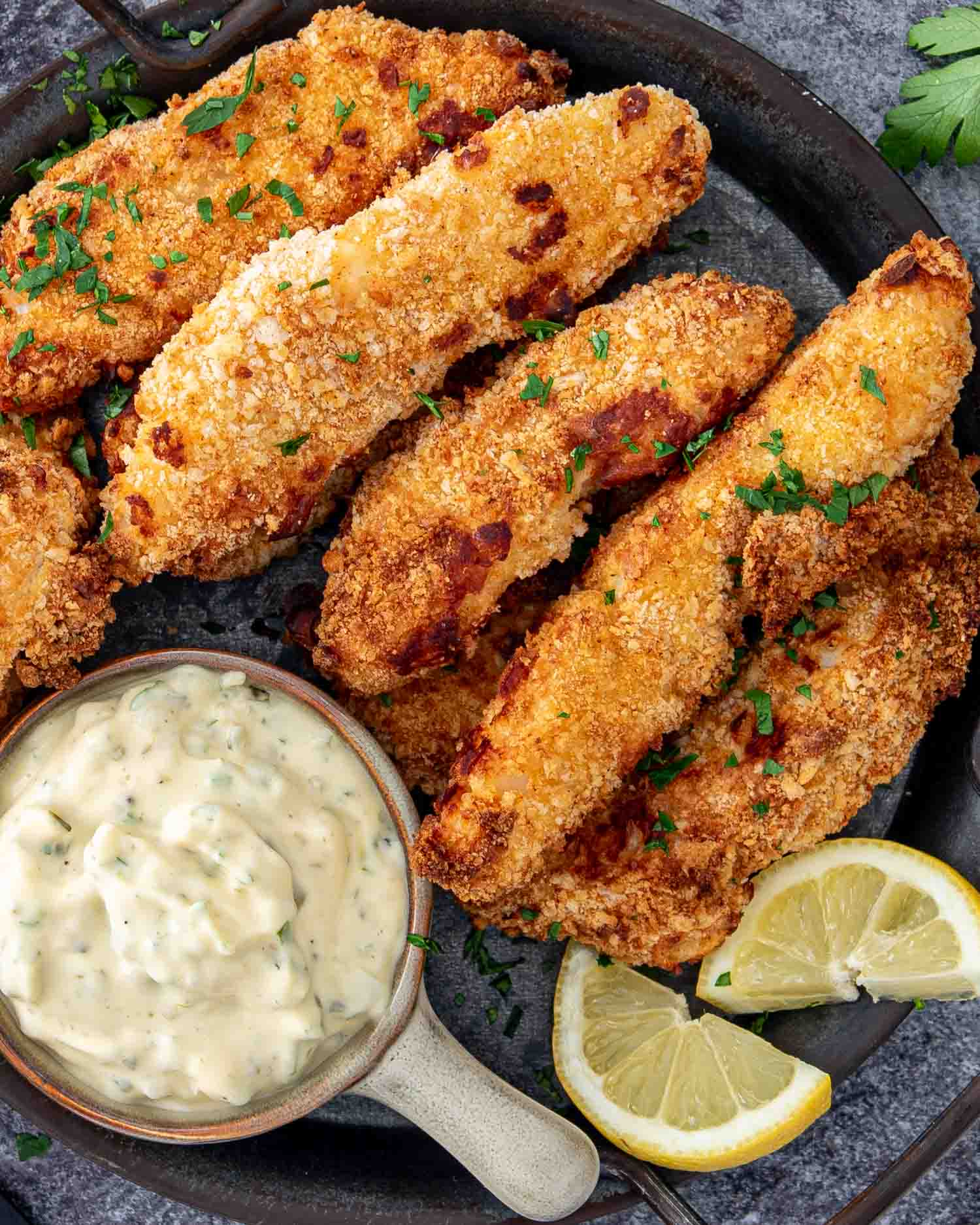 air fried fish sticks on a platter with a bowl with tartar sauce in it.