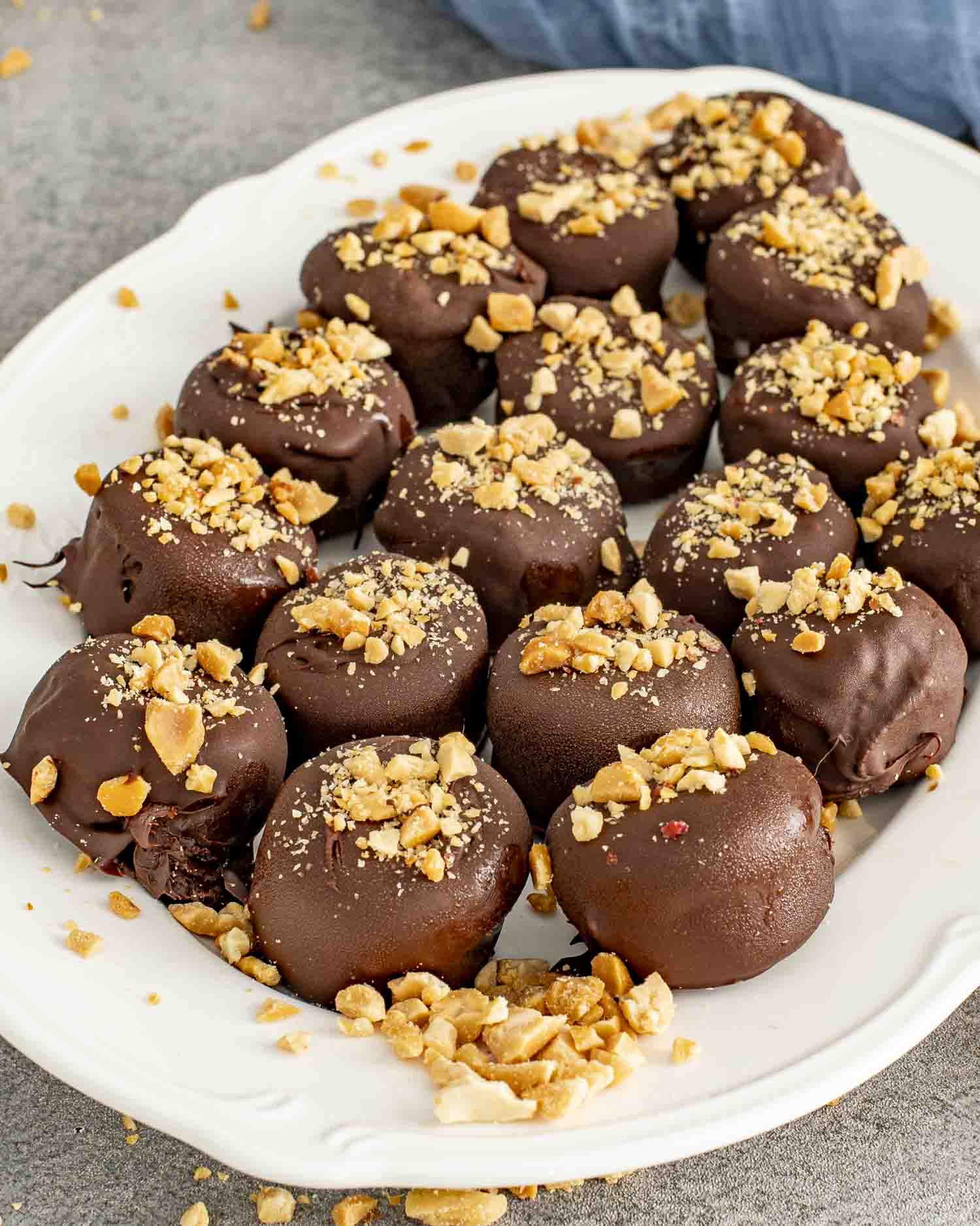 White serving platter filled with frozen chocolate-dipped banana bites sprinkled generously with crushed nuts for a sweet snack.