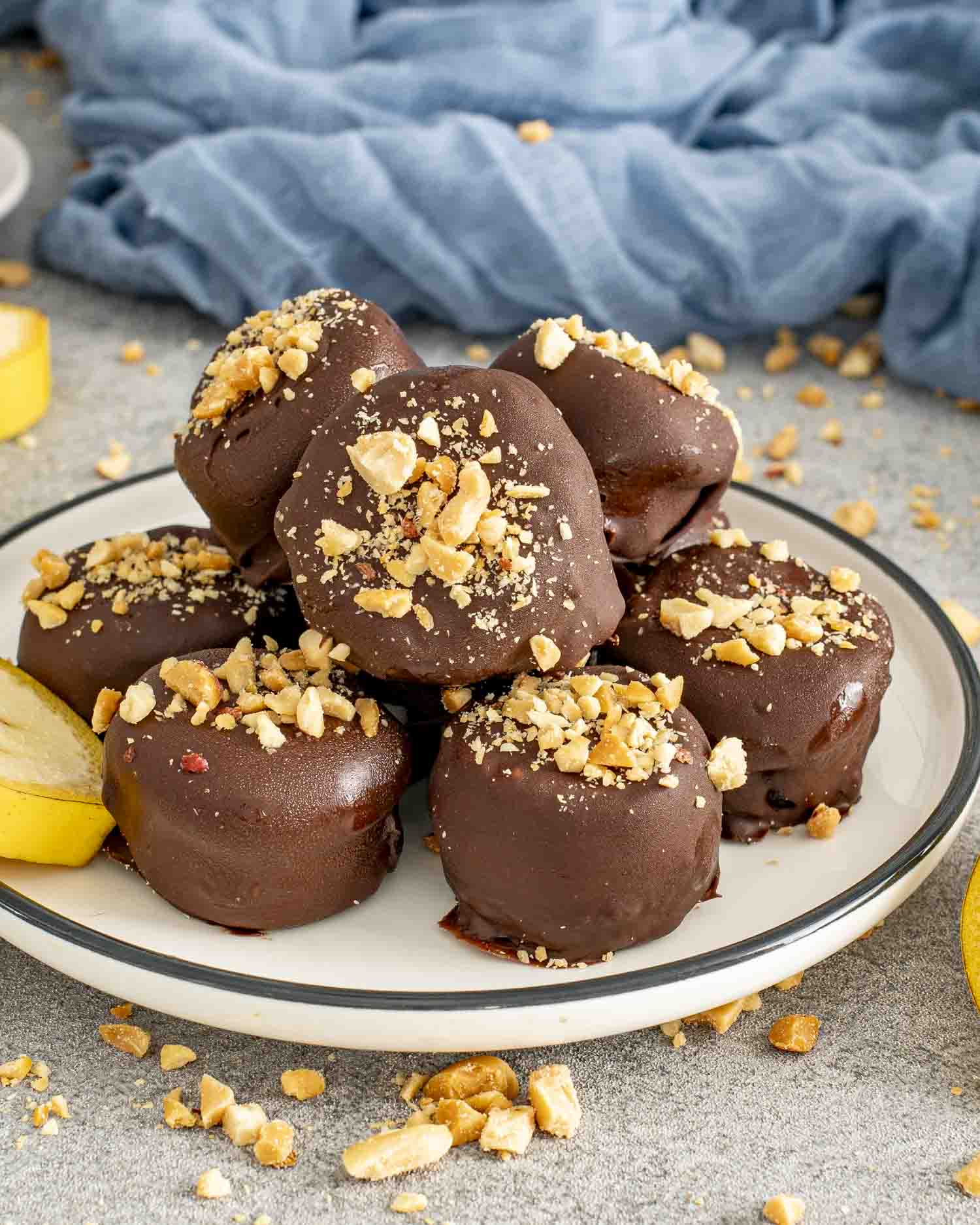 Plate piled with frozen chocolate banana bites coated in rich chocolate and topped with chopped peanuts for crunch.