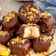 Stack of frozen chocolate-covered banana bites sprinkled with crushed nuts, one showing creamy banana center on a plate.