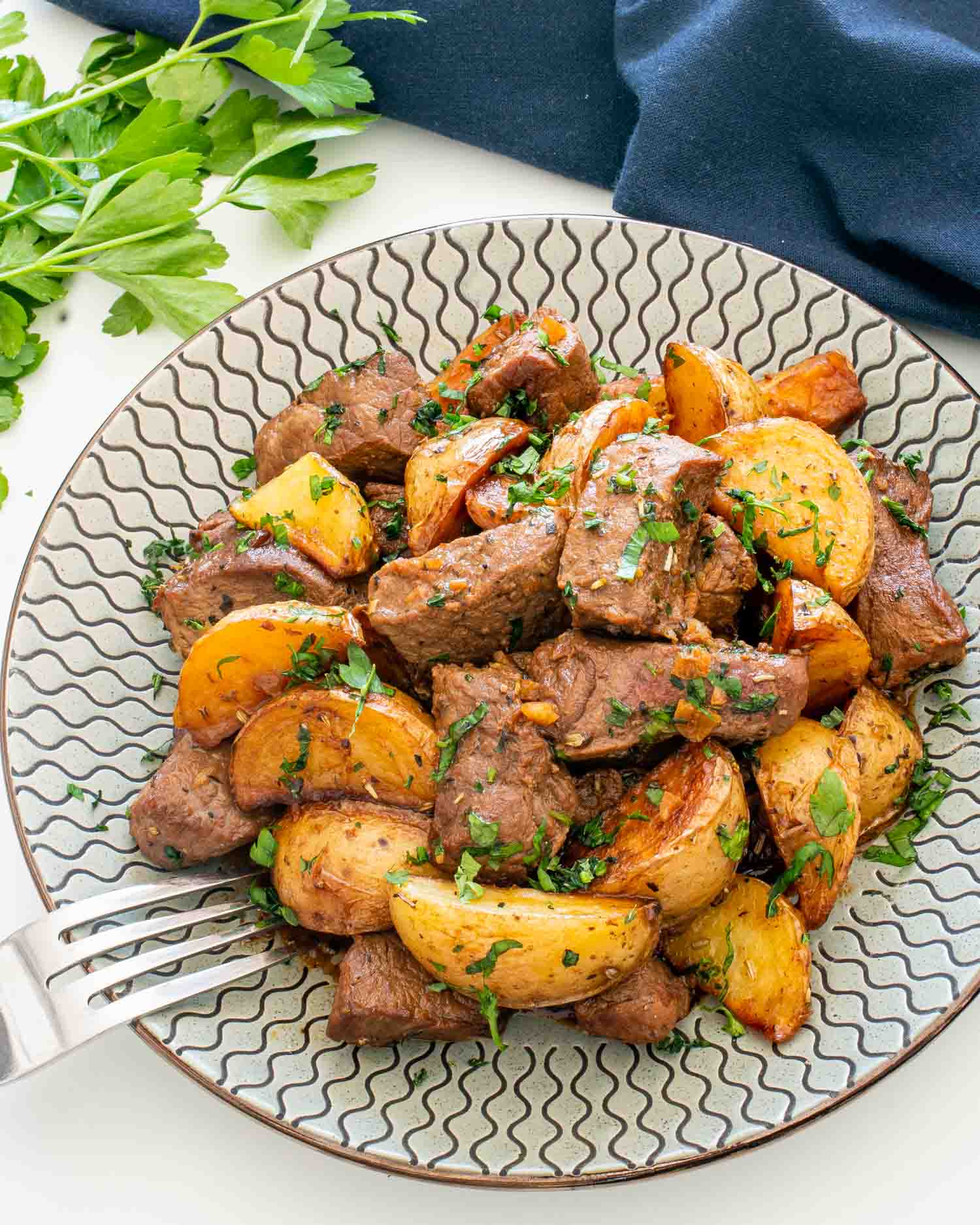 garlic butter steak and potatoes serving on a plate garnished with parsley.